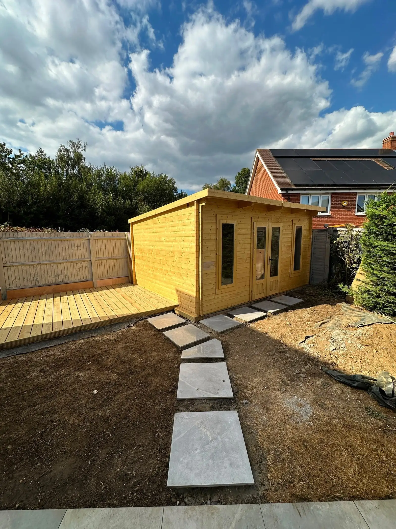 New timber garden room with full-height glazing, decking and stone stepping-stone path across the lawn