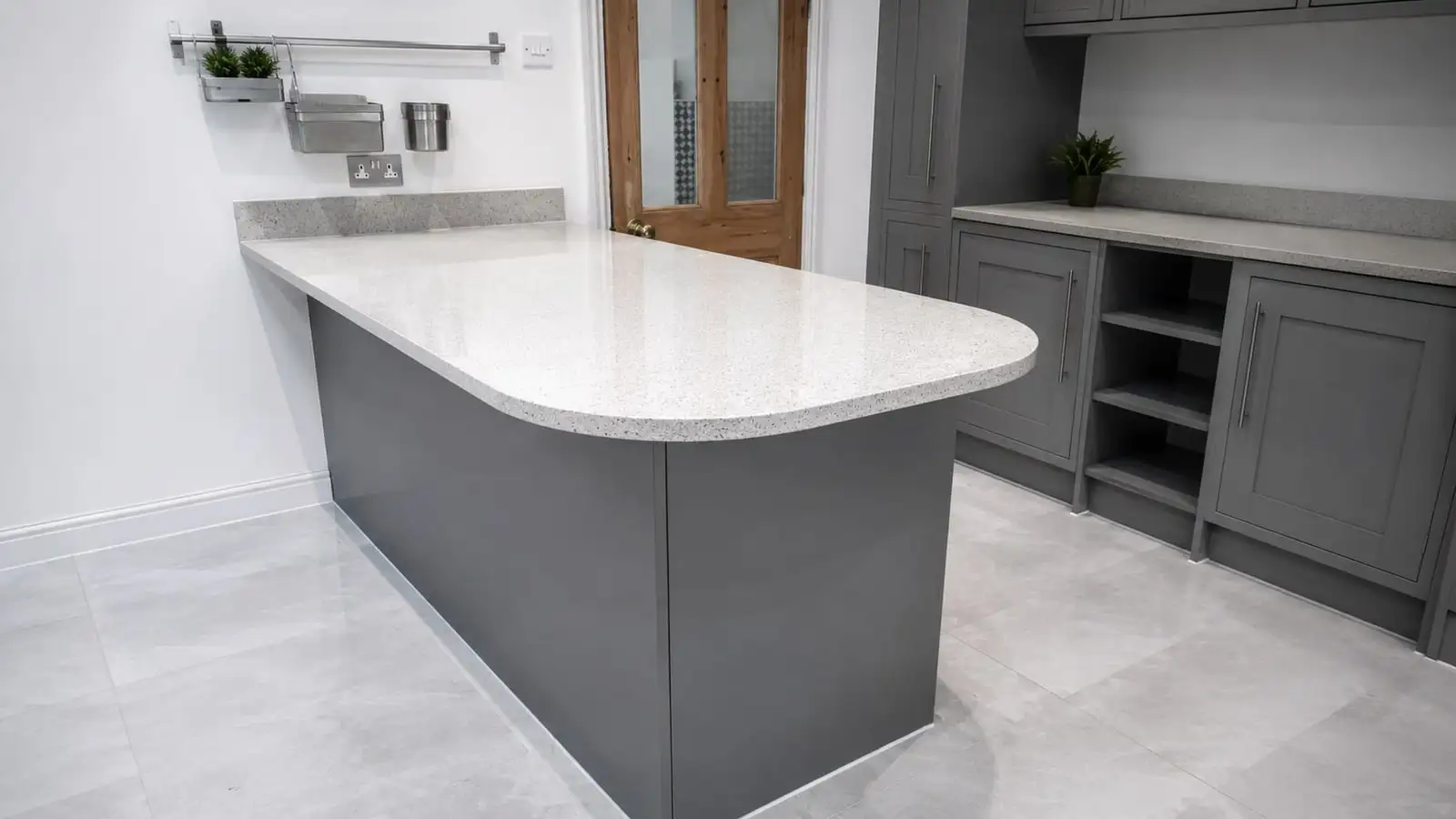 Fitted kitchen with curved quartz island, grey shaker units and large-format floor tiles