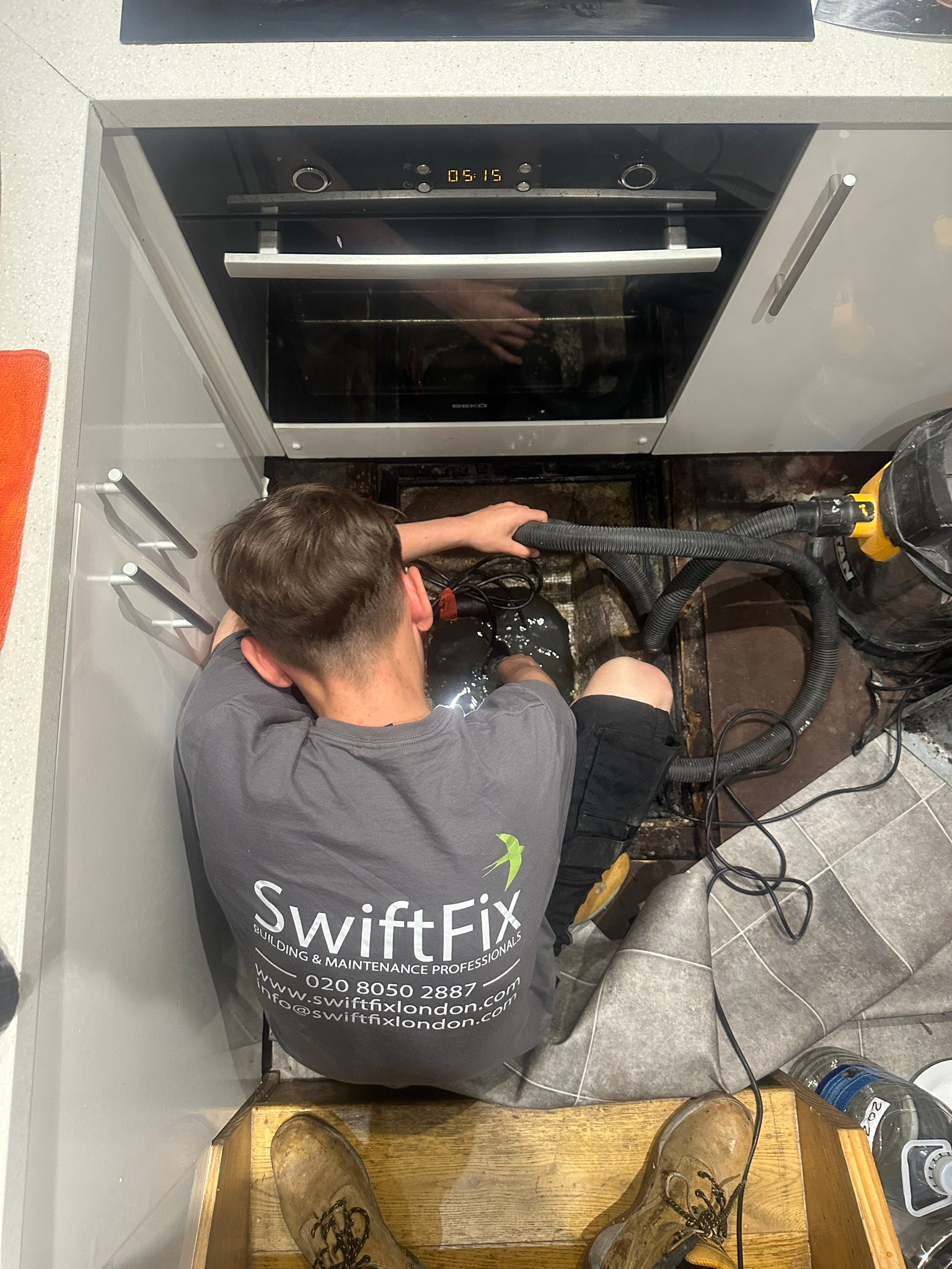 SwiftFix London tradesman installing appliance or plumbing under a kitchen counter.