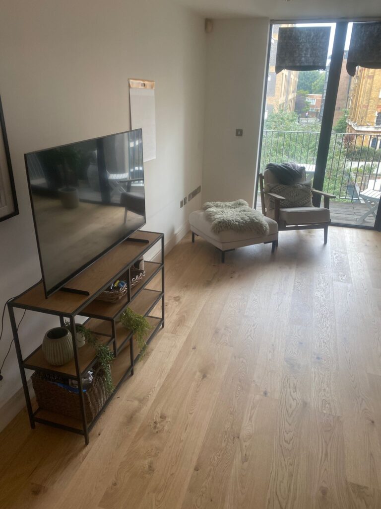 Refurbished living room by SwiftFix London with wooden flooring, TV stand, and balcony doors letting in natural light.