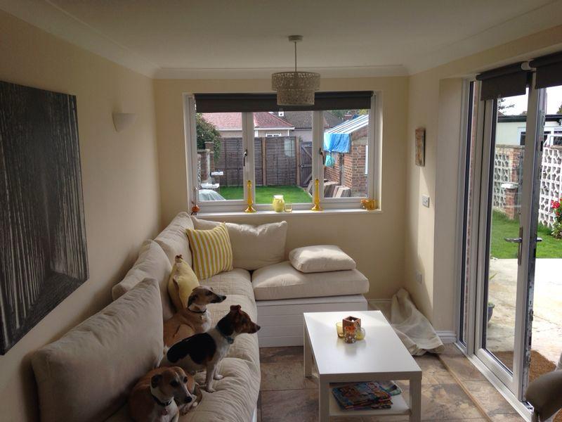 home renovations -Cosy living room renovated by SwiftFix London featuring cream sofa, dogs, and sliding glass doors opening to the garden.