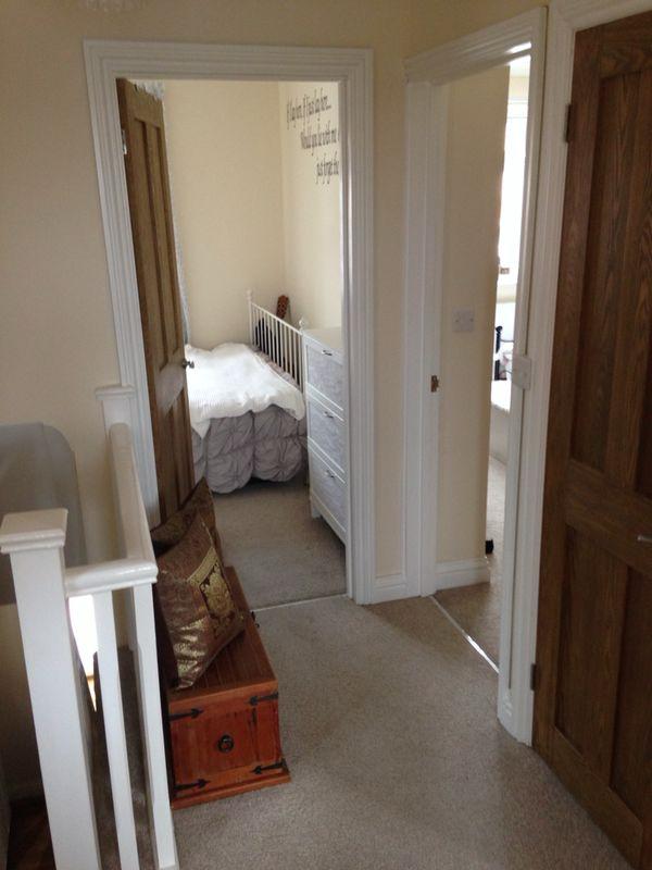 Upstairs landing of renovated home by SwiftFix London showing carpeted hallway, wooden door, and bedroom.